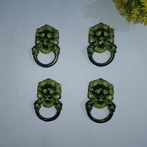 Könnte beinhalten: Vier grüne Türklinken mit Löwenkopf und Ringgriff. Die Löwenköpfe sind mit schwarzen Augen und einem goldenen Rand verziert.