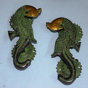 May include: A pair of decorative door handles in the shape of fish. The handles are made of brass and have a green and gold finish.