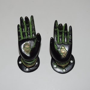 May include: A pair of black and green hand-shaped door handles with gold accents. The handles are mounted on round black bases with holes for screws.