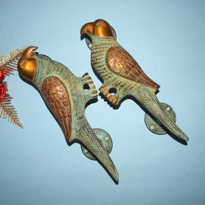 May include: A pair of ornate brass door handles shaped like parrots. The handles are a combination of green and gold with intricate details.