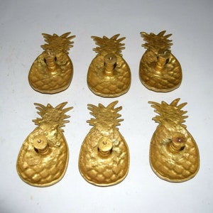 May include: Six gold pineapple-shaped cabinet knobs with a textured surface. Each knob has a small round hole in the center for mounting.