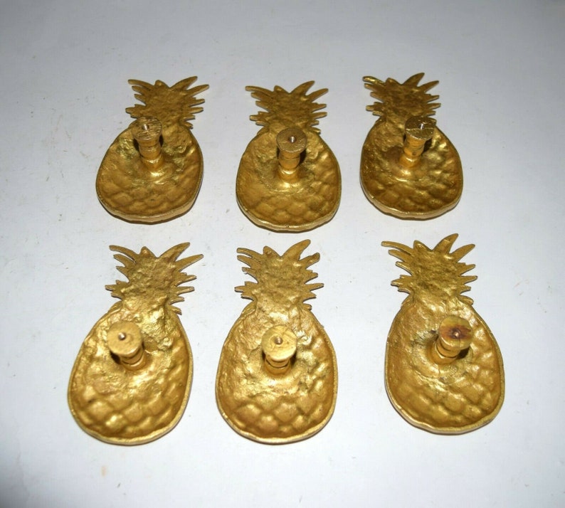 May include: Six gold pineapple-shaped cabinet knobs with a textured surface. Each knob has a small round hole in the center for mounting.