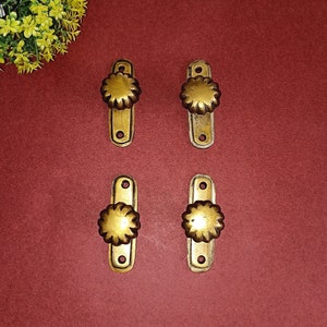Könnte beinhalten: Vier goldfarbene Schrankknöpfe mit einem dekorativen Blumenmuster. Jeder Knopf ist an einer rechteckigen Platte befestigt.