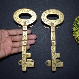 May include: Two ornate brass keys with intricate floral designs. The keys are about 10 inches long and have a keyhole at the top. The keys are a golden color and have a shiny finish.