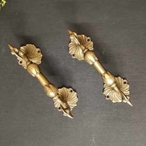 May include: Two ornate brass door handles with a floral design. The handles are in the shape of a stylized bird with a long, pointed beak.
