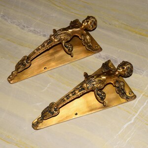May include: Two gold-toned metal door handles shaped like a winged cherub. Each handle is attached to a triangular base.