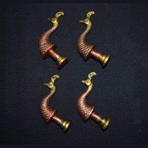 Könnte beinhalten: Satz von vier Türklinken in Form eines Pfaus mit einer Kupfer- und Goldoberfläche. Die Knöpfe sind mit einem strukturierten Muster verziert und haben eine runde Basis.