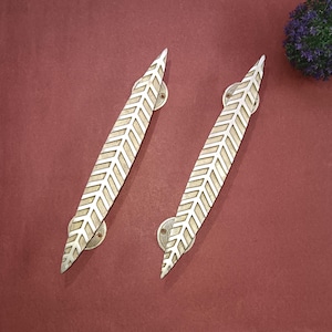 以下が含まれることがあります： 幾何学模様の入った銀色の葉の形をしたドアノブが2つ。ノブは赤い背景の上にあります。