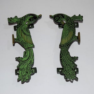 Może przedstawiać: Para ozdobnych klamki do drzwi w kształcie pawia. Klamki są wykonane z mosiądzu i mają zielono-czarne wykończenie.