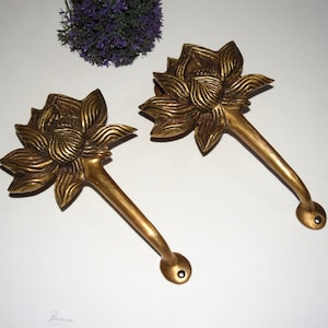 Puede incluir: Dos tiradores de puerta de latón adornados con forma de flor de loto. Los tiradores están detallados con tallas intrincadas y tienen un acabado dorado.