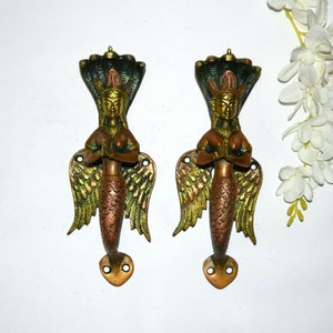 Könnte beinhalten: Ein Paar verzierte Messing-Türgriffe in Form einer Meerjungfrau mit Flügeln. Die Griffe sind gold- und kupferfarben mit einer grün-blauen Krone auf dem Kopf jeder Meerjungfrau.
