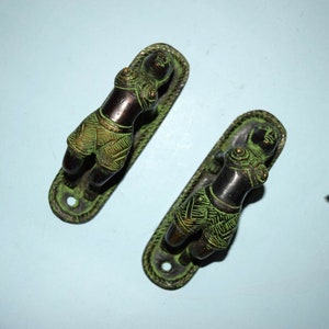 May include: A pair of decorative door handles with a green patina finish. Each handle features a stylized figure with intricate details.