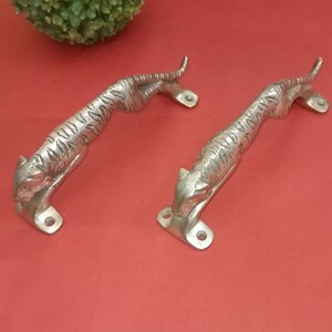 May include: Two silver tiger door handles with a detailed design. The handles are made of metal and have a polished finish.
