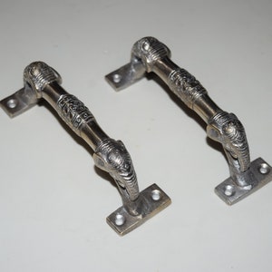 Puede incluir: Dos tiradores de puerta plateados con diseños de cabeza de elefante. Los tiradores son de metal y tienen un acabado pulido.