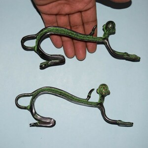 Op de afbeelding: Twee antieke bronzen decoratieve objecten in de vorm van een aap. De apen bevinden zich in een kruipende positie met een groene streep over hun rug. De objecten hebben een donkerbronzen afwerking en worden getoond op een lichtblauwe ondergrond.