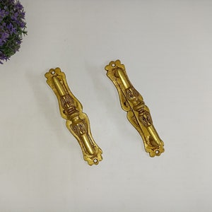May include: Two ornate gold-toned metal drawer pulls with intricate floral designs.