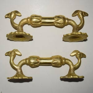 May include: Two pairs of ornate brass door handles with a decorative floral design. Each handle features a curved, stylised bird-like shape on each end.