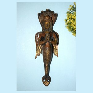 May include: A brass door handle shaped like a mermaid with a cobra head and wings. The mermaid is in a prayer position with her hands clasped together.