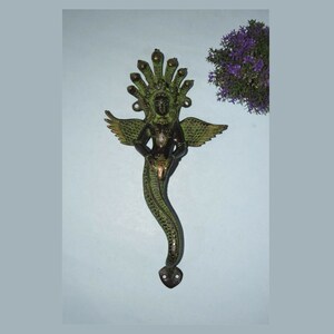 May include: A green and gold brass door handle featuring a winged serpent figure holding a small figure in its hands. The serpent has a multi-headed hood.
