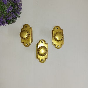 May include: Three gold-toned door knobs with a decorative floral design. Each knob is rectangular with a raised, round centre.
