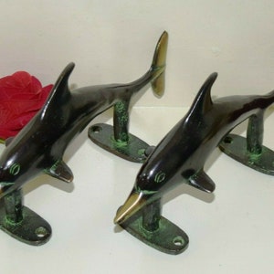 Könnte beinhalten: Zwei schwarze und grüne Metall-Delfin-Türgriffe mit goldener Oberfläche. Die Delfine sind in einer springenden Pose mit nach oben gerichteten Schwänzen.