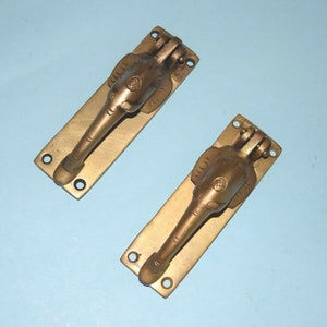 May include: Two gold-toned door knockers shaped like elephants with intricate details. The knockers are mounted on rectangular plates.