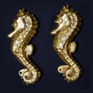 May include: Two gold seahorse sculptures with detailed textures and a metallic finish. The seahorses are side-by-side against a dark background, showcasing their intricate design and aquatic theme.
