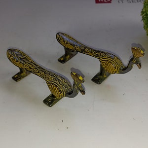 Könnte beinhalten: Zwei verzierte Messing-Türgriffe in Form von Pfauen mit gelben und schwarzen Details.