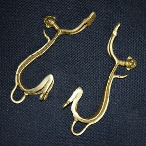 May include: Two gold-colored metal hooks with decorative details. Each hook has a curved shape and a small, round knob at the top.