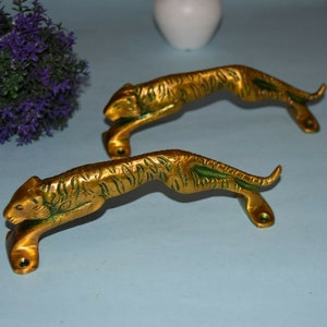 May include: Two gold-colored tiger door handles with green accents. The handles are shaped like tigers in a leaping pose.