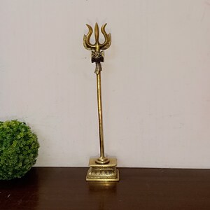 May include: A gold-colored metal trident with a decorative base. The trident is a traditional Hindu symbol.
