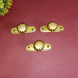 Könnte beinhalten: Drei goldfarbene Schubladenknöpfe mit einem dekorativen Blumendesign. Jeder Knopf hat zwei Löcher zur Montage.