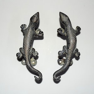 May include: A pair of antique bronze lizard door handles with a distressed finish. The lizards are facing opposite directions and have detailed scales.