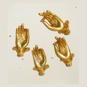 Puede incluir: Cuatro tiradores de puerta de metal de color dorado en forma de mano con diseños intrincados. Los tiradores tienen la forma de una mano con los dedos curvados hacia adentro.