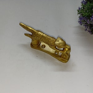 Può includere: Un batacchio per porta in metallo dorato a forma di animale stilizzato, forse un gatto o un cane, con la testa girata di lato. Il batacchio è montato su una base rettangolare con un design decorativo.