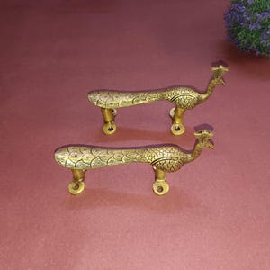 Peut inclure: Deux poignées de porte en forme de paon dorées avec des détails complexes. Les poignées sont en métal et ont une finition polie.