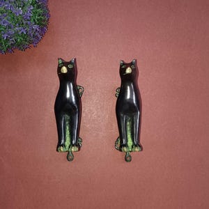 May include: Two black cat-shaped door handles with gold accents. The handles are made of metal and have a shiny finish.