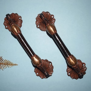 May include: Two ornate door handles with a floral design. The handles are made of dark brown metal with gold accents.