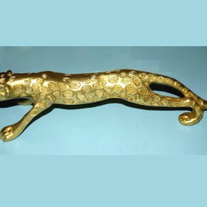 May include: A gold-colored metal sculpture of a leopard in a crouching position. The sculpture is detailed with a spotted pattern.