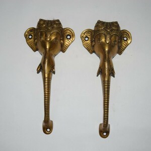May include: A pair of gold-toned door handles shaped like the head of an elephant with intricate details. The handles are made of metal and have a traditional Indian design.