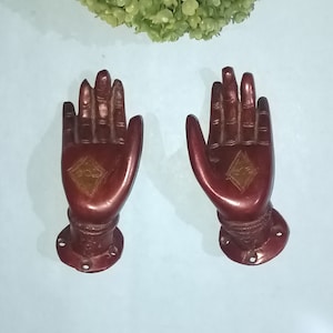 May include: Two ornate, red-brown, hand-shaped door handles with a diamond-shaped design in the centre of each palm.