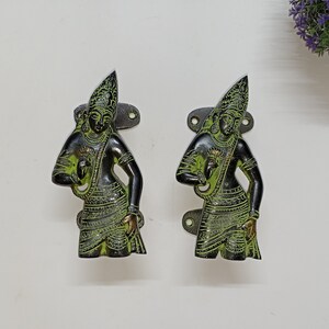 May include: Two antique brass door handles with green patina. Each handle features a detailed figure of a person in traditional clothing.