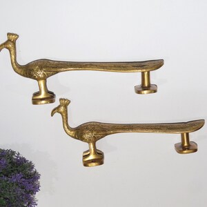 May include: Two gold peacock door handles with intricate details. The handles are made of brass and have a traditional Indian design.