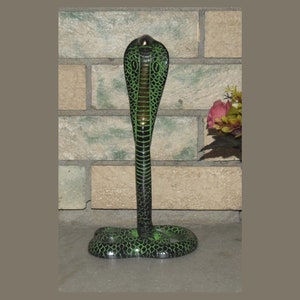 Op de afbeelding: Een groene en zwarte cobra-beeld met een opgeheven kap. Het beeld is gemaakt van metaal en heeft een gedetailleerd ontwerp.