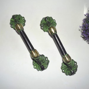 May include: Two black and green door handles with a lotus flower design. The handles are made of metal and have a polished finish.