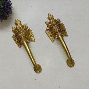 Può includere: Due maniglie per porte in ottone con un design a testa di elefante. Le maniglie dorate presentano dettagli intricati sul viso e sull'acconciatura dell'elefante. Sono montate su una superficie bianca.