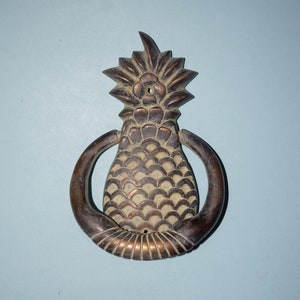 Puede incluir: Un llamador de puerta de bronce con forma de piña y un asa de anillo.