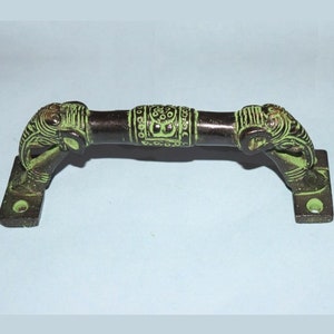 Puede incluir: Una manilla de puerta de metal verde y marrón con terminales de cabeza de elefante. La manilla está decorada con un patrón repetitivo de círculos y puntos.