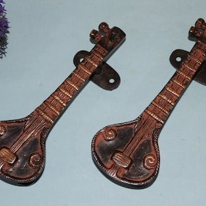 May include: Two antique-style door handles shaped like sitar musical instruments. The handles are made of metal and have a dark brown finish with gold accents.