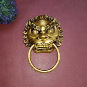 以下が含まれることがあります： リングハンドルが付いた金色のライオンの頭のドアノッカー。ノッカーは、複雑な彫刻と獰猛な表情で詳細に描かれています。